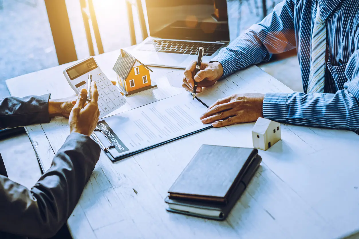 Two people signing property management documents with a model house in the background, symbolizing local expertise in NJ & PA property management